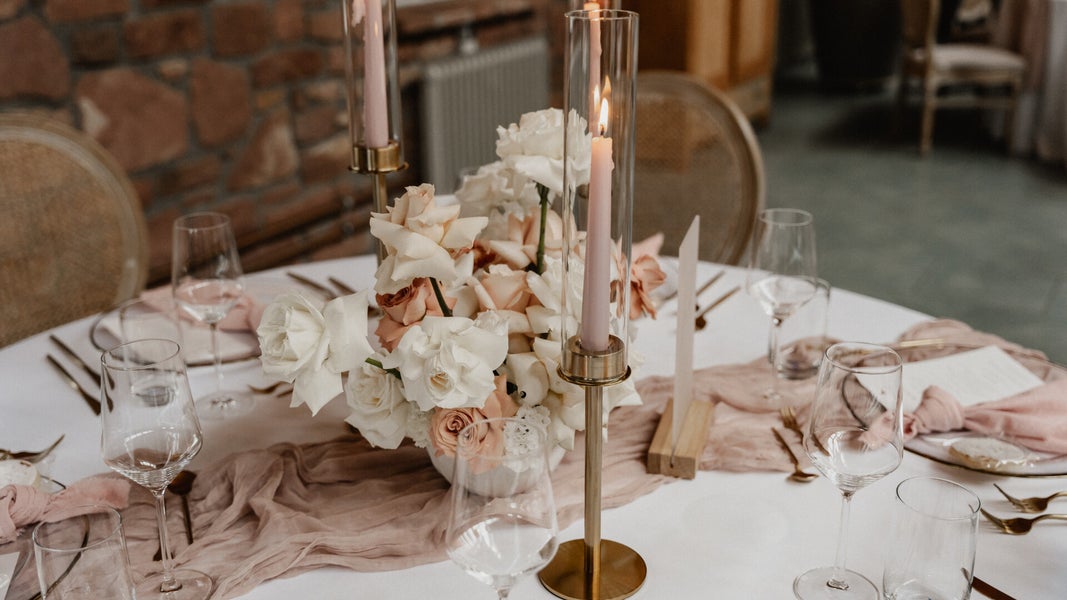 Eleganter gedeckter Tisch mit Blumenmittelstück, Kerzen in Glashüllen und edlem Geschirr
